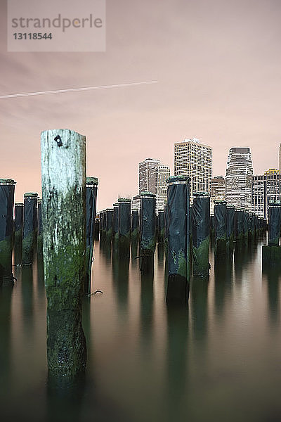 Holzpfosten im East River gegen beleuchtete Gebäude