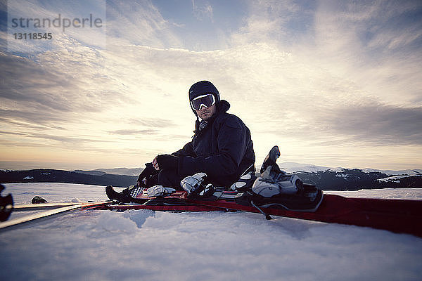 Porträt eines Skifahrers  der auf einer verschneiten Landschaft vor dem Himmel sitzt