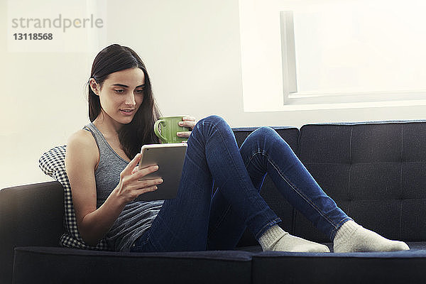 Frau sitzt auf dem Sofa und benutzt ein digitales Tablet