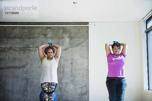 Zuversichtliche Freunde benutzen Hanteln beim Üben an der Wand im Yogastudio