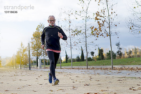 Joggen eines älteren Mannes in voller Länge  während er im Herbst im Park trainiert