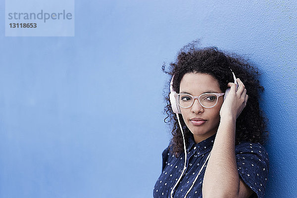 Nachdenkliche junge Frau  die Musik vor blauem Hintergrund hört