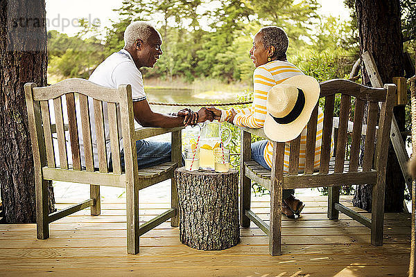 Älteres Ehepaar hält Hände  während es auf Stühlen am See sitzt