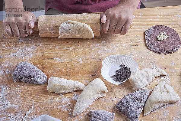 Geschnittene Hände eines Jungen  der auf einer Kücheninsel Teig rollt