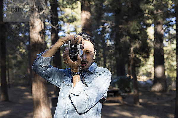 Mann fotografiert mit Kamera gegen Bäume im Wald