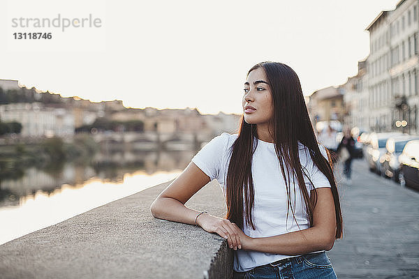 Nachdenkliche junge Frau schaut weg  während sie am Kanal in der Stadt steht