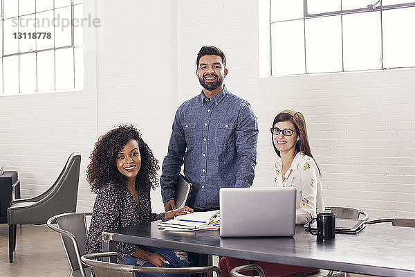 Porträt von selbstbewusst lächelnden Geschäftsleuten bei Tisch im Büro
