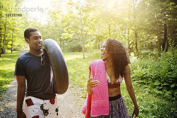 Fröhliches Paar mit aufblasbarem Ring und Handtuch geht auf einem Waldweg