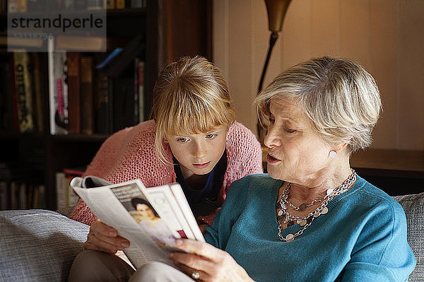 Großmutter liest Zeitschrift  während sie zu Hause auf dem Sofa sitzt