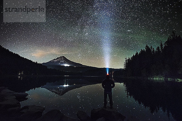 Silhouetten-Mann mit Scheinwerfer steht am Seeufer vor Sternenhimmel