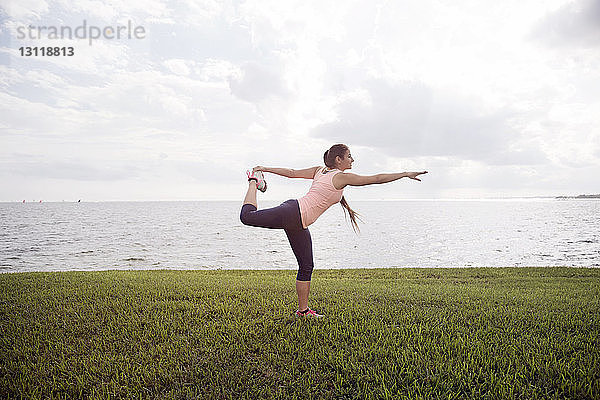 Seitenansicht einer Frau  die auf einem Grasfeld gegen das Meer trainiert