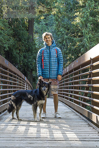 Porträt eines glücklichen Mannes mit Hund auf einem Steg im Wald stehend