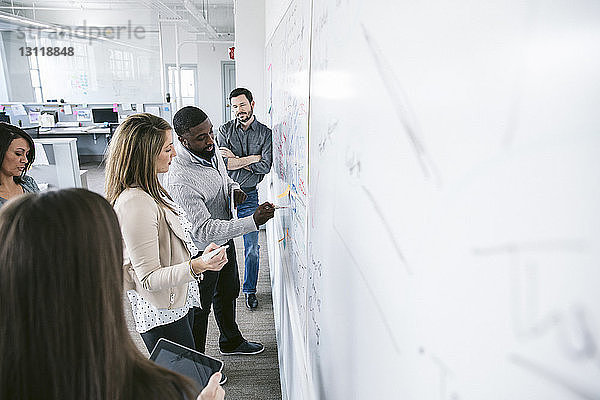 Geschäftsmann erklärt Kollegen  während er im Büro am Whiteboard schreibt