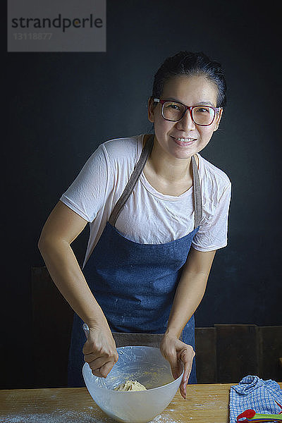Porträt einer lächelnden Frau  die in der Küche Teig in einer Schüssel rührt