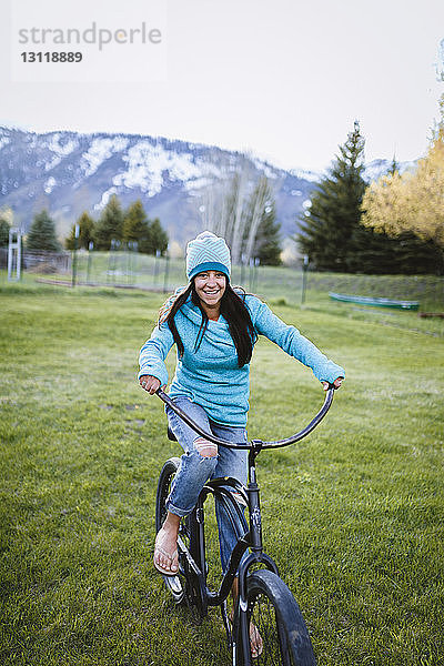 Porträt einer Fahrrad fahrenden Frau auf einem Grasfeld gegen einen Berg im Park