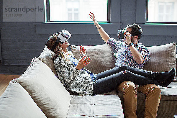 Mitarbeiter tragen Virtual-Reality-Simulatoren  während sie im Büro auf dem Sofa sitzen
