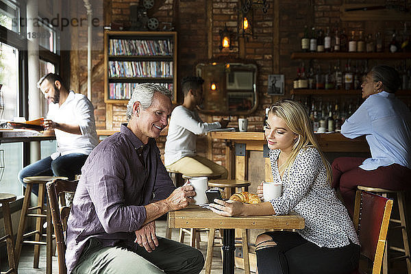 Frau zeigt Mann Telefon  während sich Kunden im Café entspannen