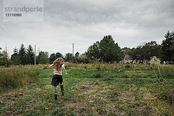 Rückansicht eines Mädchens  das auf einem Grasfeld vor bewölktem Himmel rennt