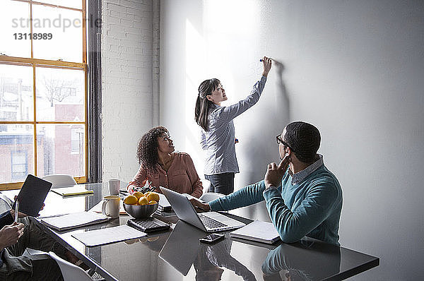 Männliche und weibliche Kollegen betrachten Geschäftsfrau beim Schreiben an der Tafel