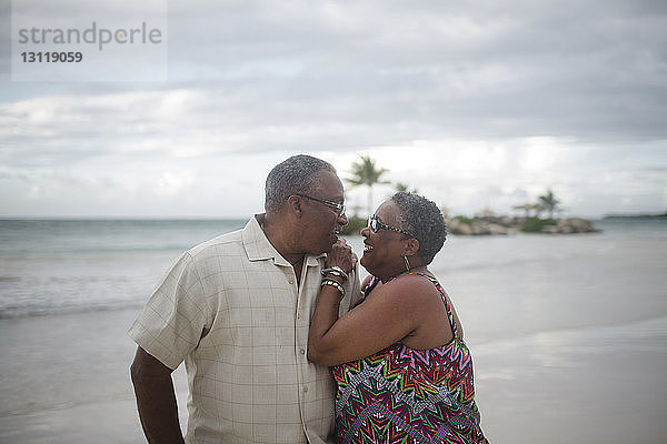 Glückliches älteres Ehepaar am Strand vor bewölktem Himmel