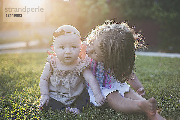 Porträt eines kleinen Mädchens  das mit seiner Schwester auf einem Grasfeld im Hinterhof sitzt