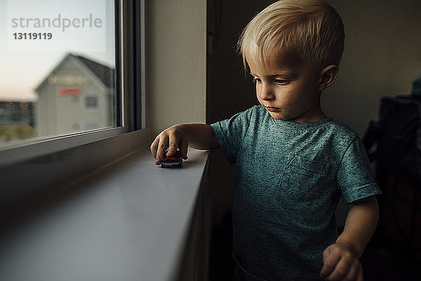 Kleiner Junge spielt zu Hause mit Spielzeugauto auf der Fensterbank