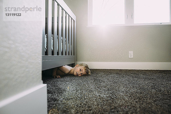 Porträt eines Jungen ohne Hemd  der zu Hause auf einem Teppich unter dem Bett liegt