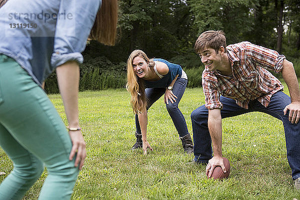 Mann hält Fussball in der Hand  während er Freundinnen auf dem Rasenplatz ansieht