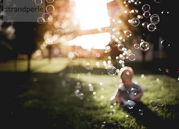 Kleiner Junge spielt im Hinterhof  während im Vordergrund Seifenblasen fliegen