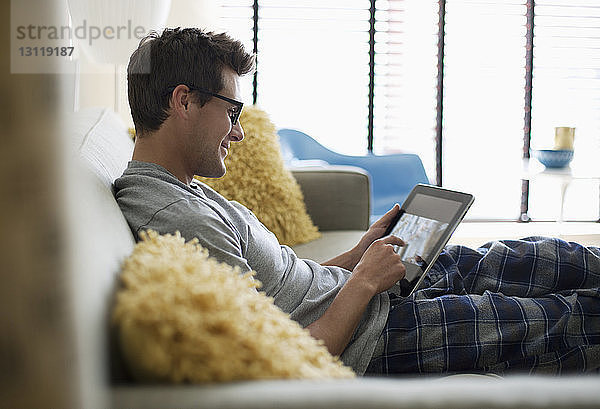 Lächelnder Mann benutzt Tablette  während er sich zu Hause auf dem Sofa ausruht