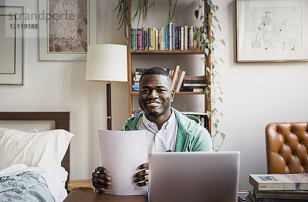 Porträt eines glücklichen Mannes  der bei der Arbeit zu Hause Dokumente in der Hand hält