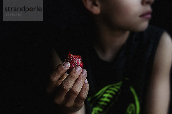 Mittendrin ein Junge  der eine Erdbeere hält  während er in einem dunklen Raum sitzt