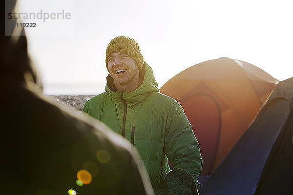 Glücklicher Mann in warmer Kleidung steht am Zelt gegen den Himmel