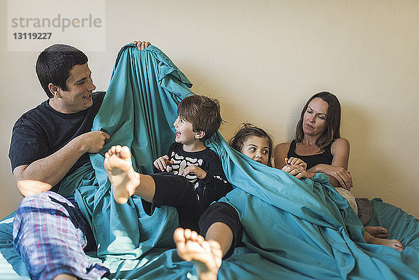 Glückliche Eltern spielen mit Kindern  während sie zu Hause im Bett sitzen