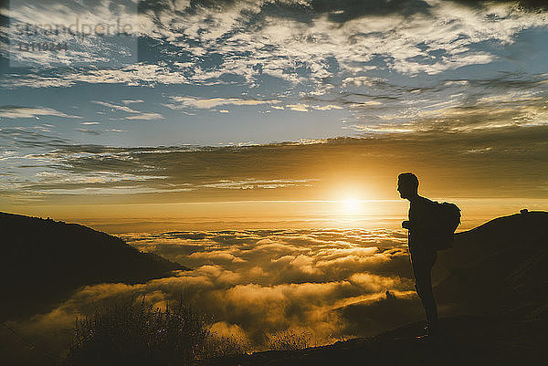 Silhouette eines männlichen Wanderers  der bei Sonnenuntergang auf einem Berg steht