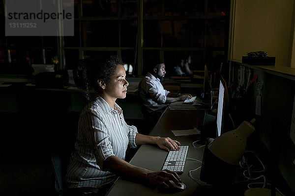 Kollegen arbeiten an Desktop-Computern am Schreibtisch in einem dunklen Büro