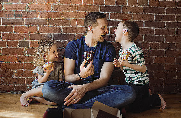 Vater mit Kindern  die Donuts essen  während sie zu Hause auf dem Boden sitzen