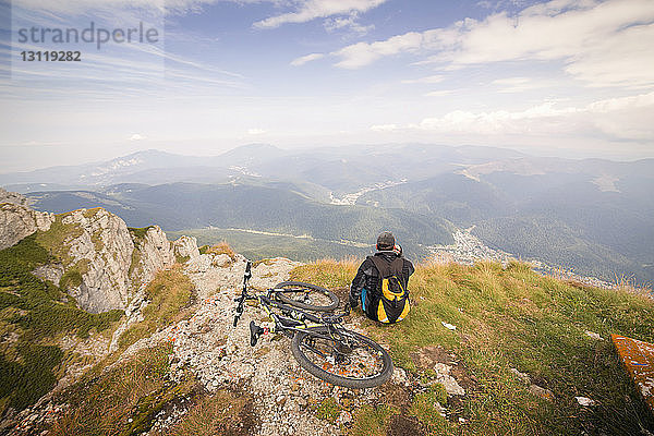 Rückansicht eines Mannes  der mit dem Fahrrad auf einem Berg sitzt