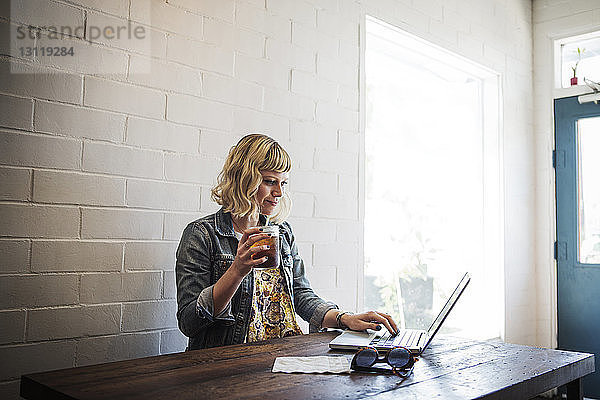 Frau benutzt Laptop  während sie im Café ein Eisteeglas hält