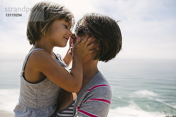 Nahaufnahme einer Mutter  die eine Tochter trägt  während sie am Strand steht