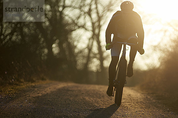 Silhouette einer Frau  die bei Sonnenuntergang auf einem Fußweg gegen den Himmel Fahrrad fährt