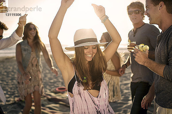 Glückliche Frau tanzt und genießt mit Freunden am Strand