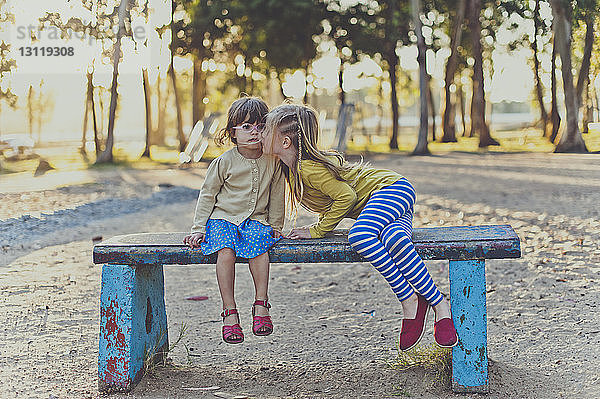 Mädchen küsst Schwester auf Parkbank sitzend
