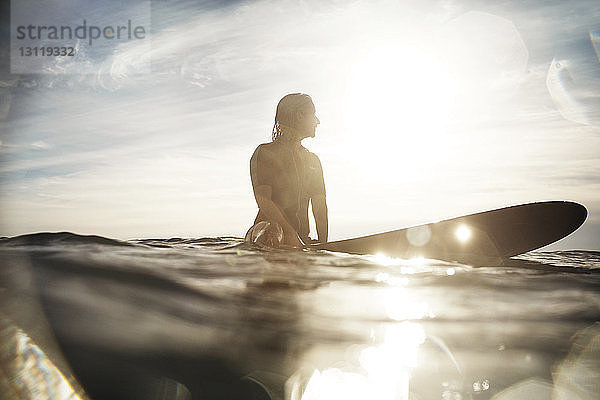 Oberflächenniveau einer Frau  die im Sommer auf einem Surfbrett im Meer sitzt