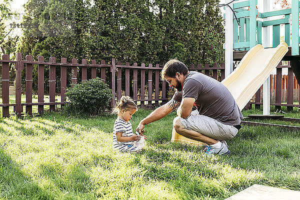 Vater spielt mit der Tochter  die auf einem Rasenfeld im Hinterhof sitzt