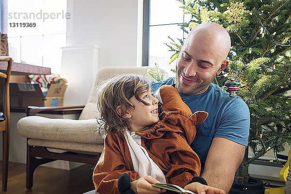 Glücklicher Vater betrachtet kostümierten Sohn zu Hause am Weihnachtsbaum