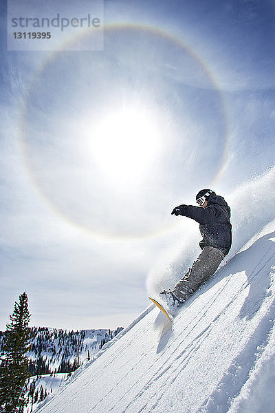 Mann beim Snowboarden auf dem Berg gegen den Himmel an einem sonnigen Tag