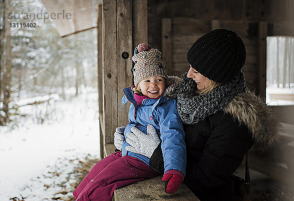 Glückliche Mutter steht neben der Tochter und sitzt im Winter am Fenster