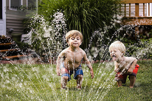 Glückliche Brüder spielen mit Sprinkler im Garten