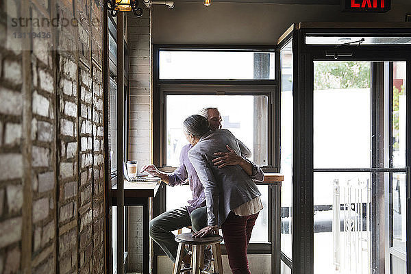 Ehepaar umarmt sich  während es im Café an den Fenstern sitzt